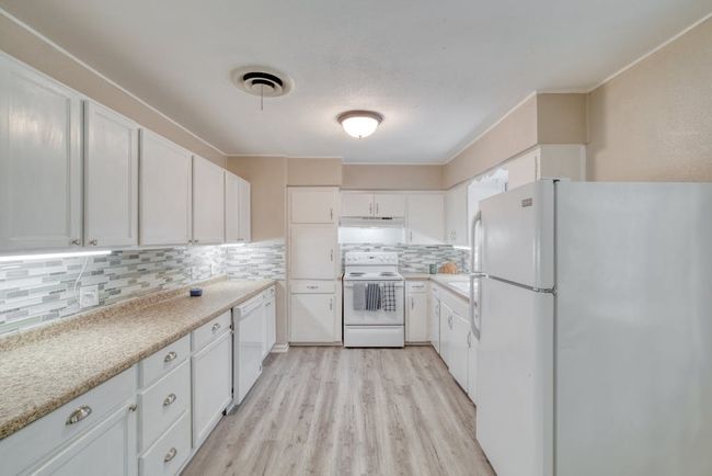 Kitchen featuring white appliances, tasteful backsplash, visible vents, white cabinets, and light wood-style flooring | Image 11