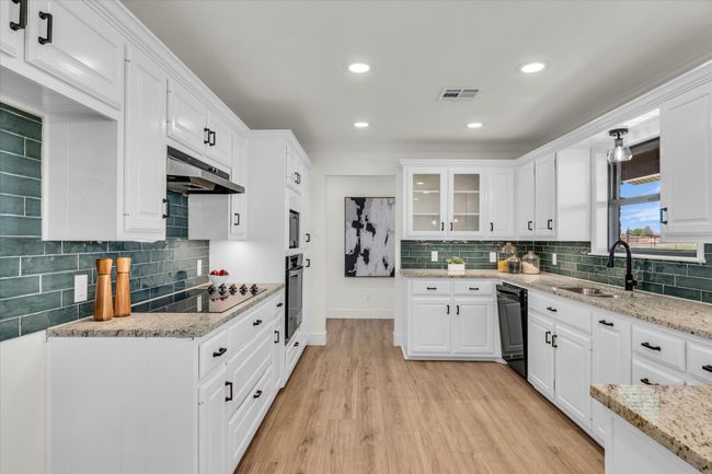 Kitchen featuring under cabinet range hood, visible vents, white cabinetry, and black appliances | Image 22
