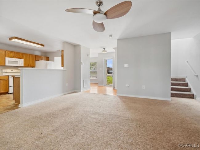 Unfurnished living room featuring light colored carpet, ceiling fan, and stairway | Image 14