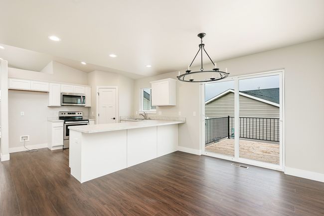 Kitchen featuring a sink, dark wood finished floors, appliances with stainless steel finishes, a peninsula, and light countertops | Image 9