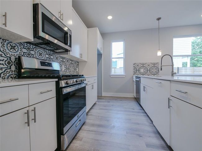 Kitchen with appliances with stainless steel finishes, backsplash, light wood finished floors, light countertops, and white cabinetry | Image 8