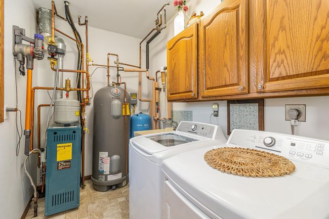 The utilities and laundry room are on the main floor. It features a brand new boiler in 2023, the well pump pressure tank & filter also in 2023, a 50 gal water heater, a utility sink, a window, cabinets & a washer & dryer. | Image 29