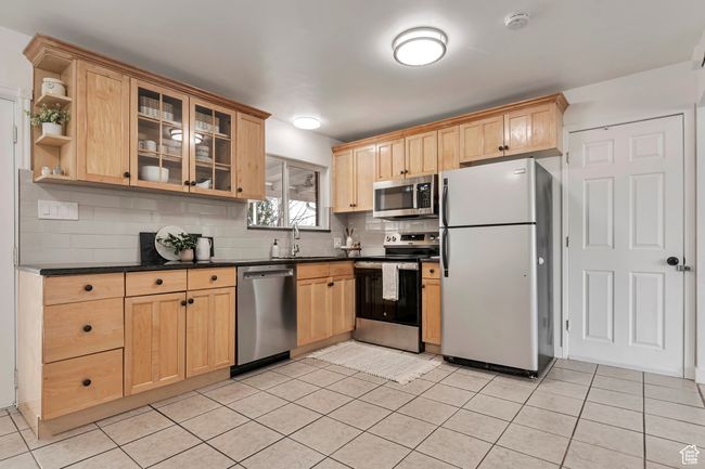 Kitchen with light brown cabinetry, a sink, dark countertops, stainless steel appliances, and decorative backsplash | Image 12
