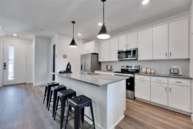 Kitchen featuring appliances with stainless steel finishes, a breakfast bar area, white cabinets, and light wood-style floors | Image 10