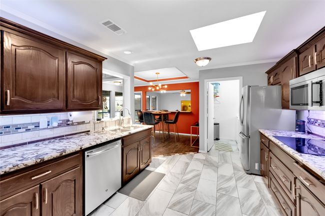 Kitchen with stainless steel appliances, a skylight, a chandelier, ornamental molding, and tasteful backsplash | Image 13
