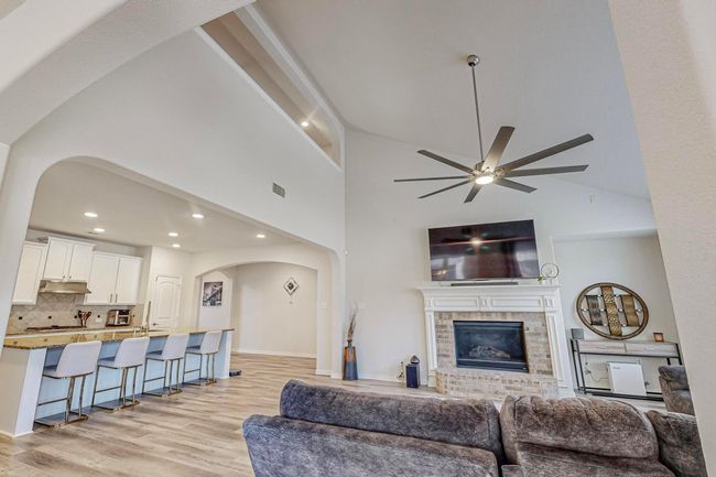 Living area with arched walkways, a brick fireplace, light wood-style floors, recessed lighting, and ceiling fan | Image 17