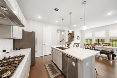 Modern, open-concept kitchen with stainless steel appliances, an island with a sink and an upgraded herringbone backsplash. The kitchen is open into the dining area with abundant natural light and a view of the side yard with NO neighbors. | Image 2