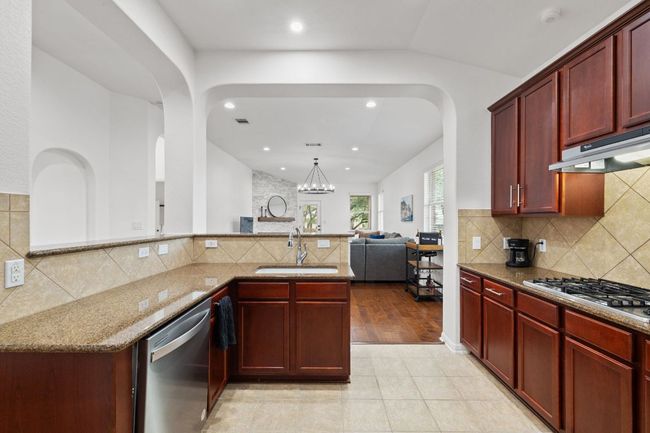Kitchen featuring dark brown cabinets, appliances with stainless steel finishes, arched walkways, light stone countertops, and decorative backsplash | Image 13