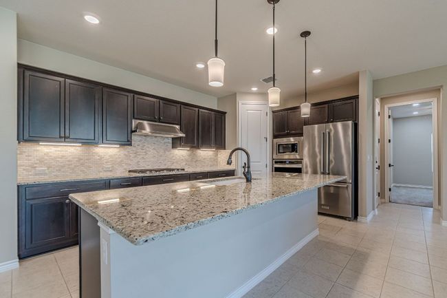 Kitchen with appliances with stainless steel finishes, light tile patterned flooring, tasteful backsplash, light stone countertops, and recessed lighting | Image 14