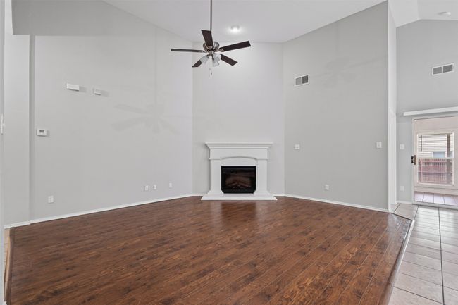 Unfurnished living room with high vaulted ceiling, a ceiling fan, wood finished floors, and a fireplace with raised hearth | Image 19