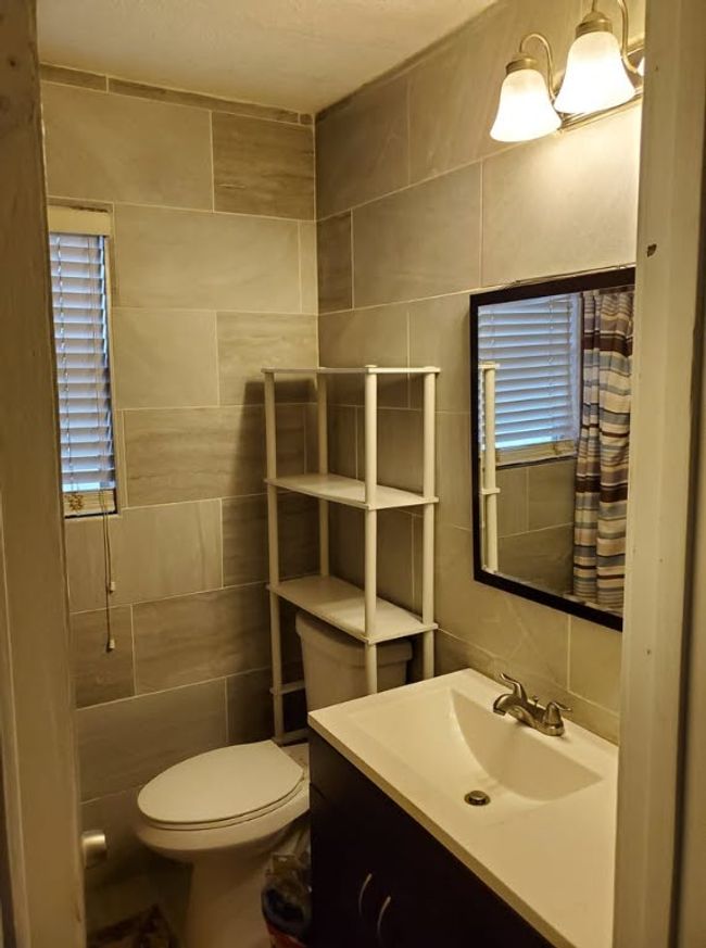 Full bathroom with tile walls, toilet, vanity, and a shower with shower curtain | Image 18