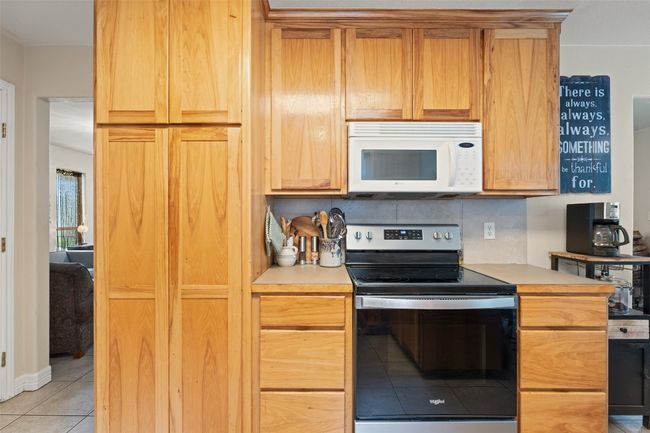 Kitchen featuring stainless steel electric range oven, white microwave, light tile patterned floors, light countertops, and backsplash | Image 21