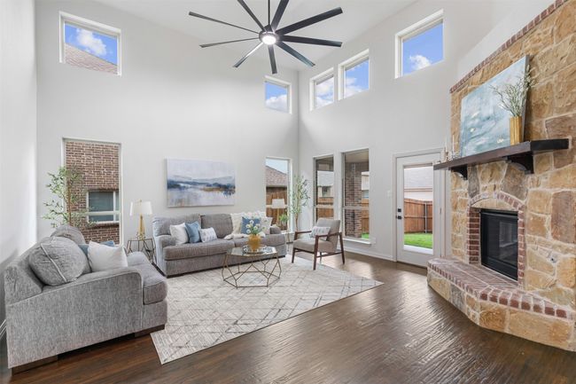 Living area with a high ceiling, a ceiling fan, wood finished floors, and a fireplace | Image 12