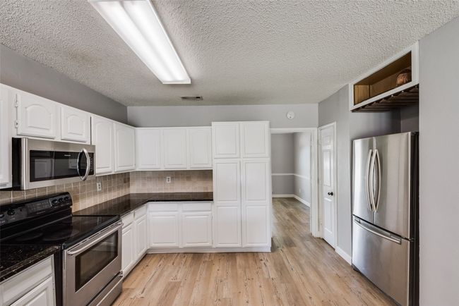 Kitchen with stainless steel appliances, white cabinets, tasteful backsplash, light wood-style flooring, and open shelves | Image 12