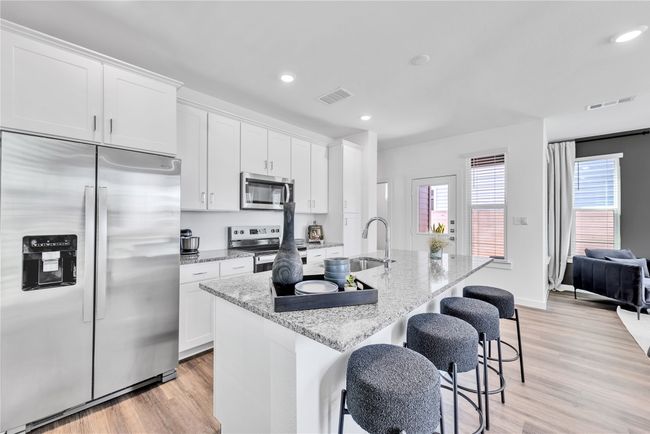 Kitchen with visible vents, appliances with stainless steel finishes, white cabinets, a sink, and an island with sink | Image 8