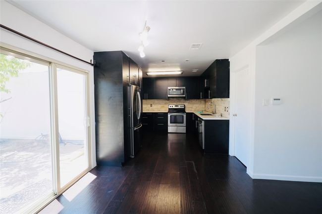 Kitchen featuring dark cabinets, light countertops, backsplash, appliances with stainless steel finishes, and dark wood-type flooring | Image 14