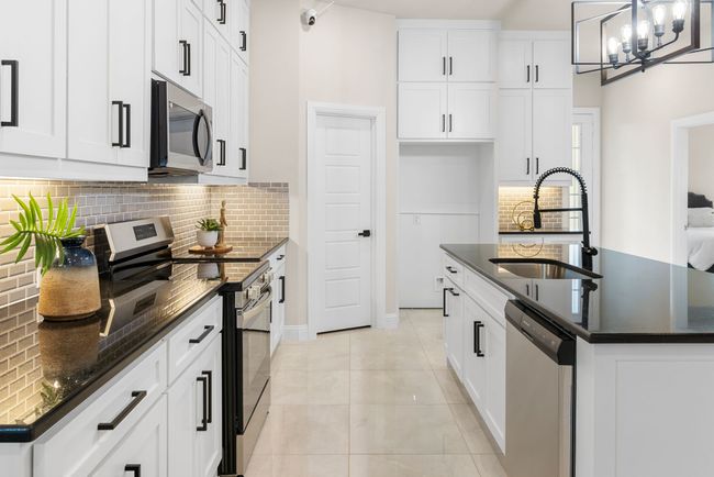 Kitchen featuring a kitchen island with sink, a sink, appliances with stainless steel finishes, an inviting chandelier, and light tile patterned floors | Image 6