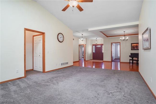 Unfurnished living room with carpet flooring, a tray ceiling, baseboards, visible vents, and ceiling fan with notable chandelier | Image 16