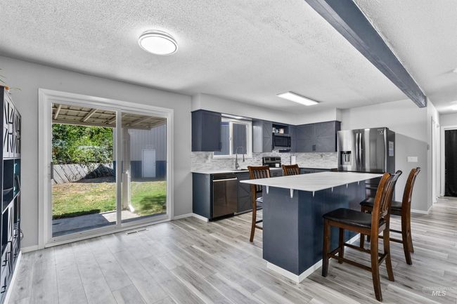 Kitchen with stainless steel appliances, a kitchen bar, light countertops, a textured ceiling, and decorative backsplash | Image 8