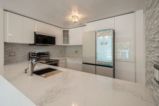 Kitchen with stainless steel electric stove, freestanding refrigerator, backsplash, light stone counters, and glass insert cabinets | Image 6