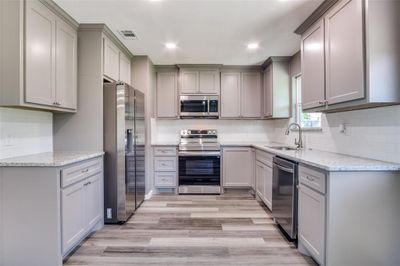 Kitchen with stainless steel appliances, light stone counters, sink, gray cabinetry, and light hardwood / wood-style floors | Image 3