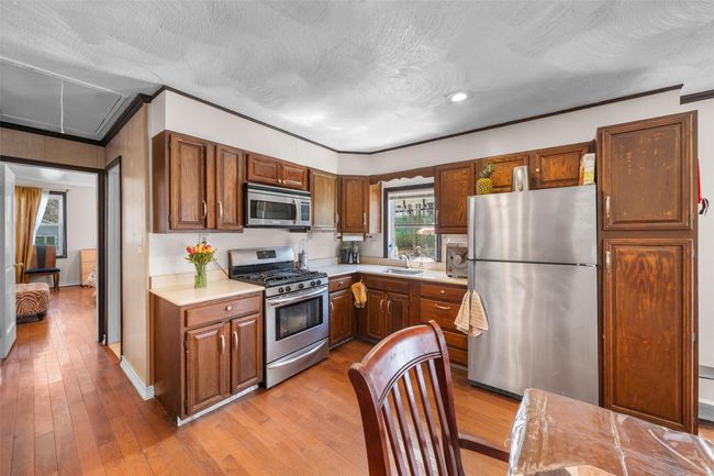 Kitchen with appliances with stainless steel finishes, light countertops, light wood-type flooring, a sink, and crown molding | Image 8