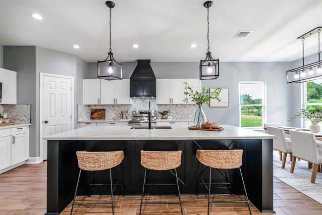 Kitchen featuring custom range hood, backsplash, a sink, light wood-type flooring, and a kitchen island with sink | Image 6