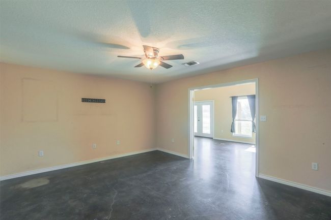 Empty room featuring finished concrete flooring, visible vents, a ceiling fan, a textured ceiling, and baseboards | Image 13