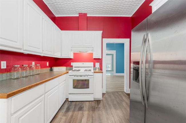 Kitchen featuring stainless steel fridge with ice dispenser, white range with gas cooktop, under cabinet range hood, white cabinetry, and light wood-style flooring | Image 16