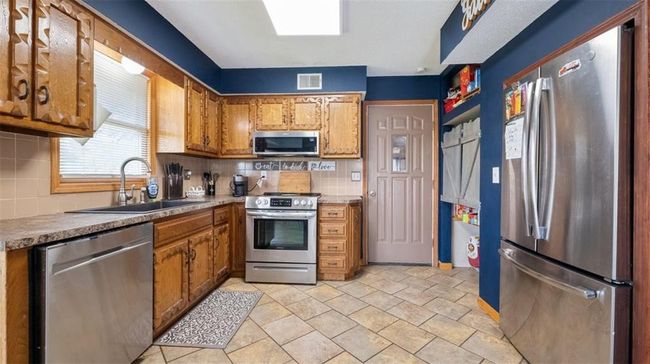 Kitchen featuring stainless steel appliances, brown cabinetry, backsplash, and light stone finish floors | Image 5