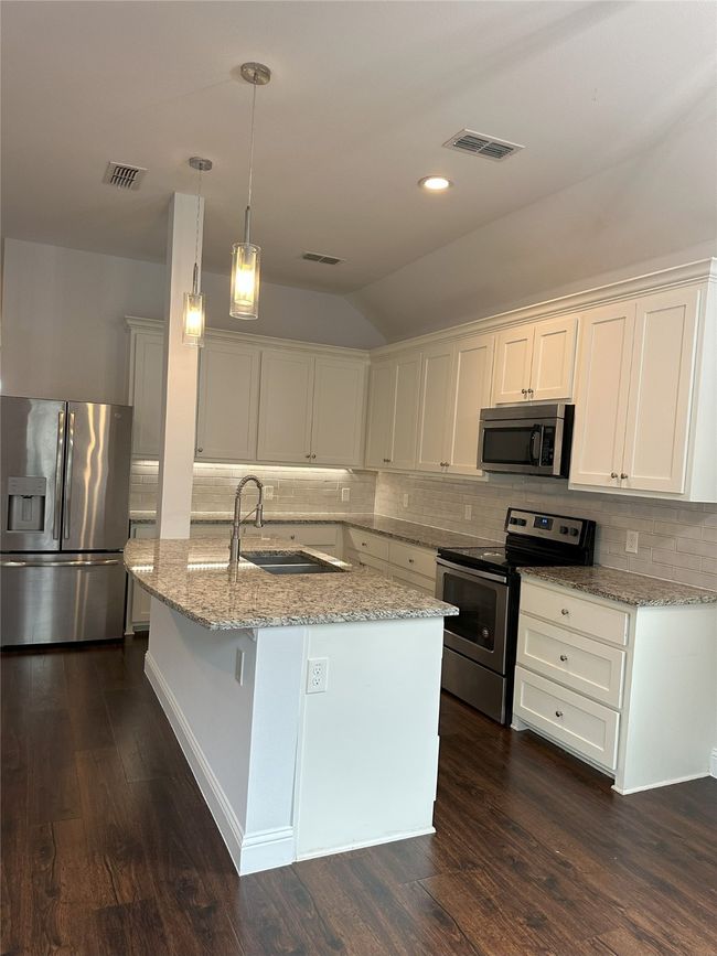 Kitchen featuring stainless steel appliances, lofted ceiling, dark wood-type flooring, backsplash, and light stone countertops | Image 6