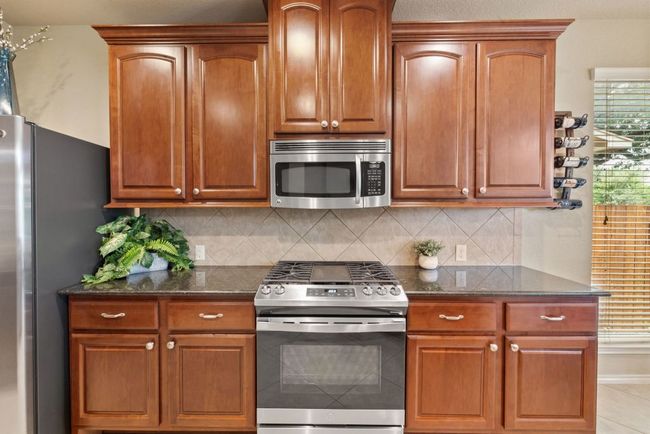 Kitchen with appliances with stainless steel finishes, dark stone counters, tasteful backsplash, and brown cabinetry | Image 10