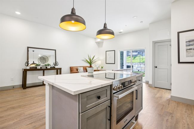 Kitchen featuring high end stainless steel range, a center island, pendant lighting, light wood-type flooring, and light stone countertops | Image 8