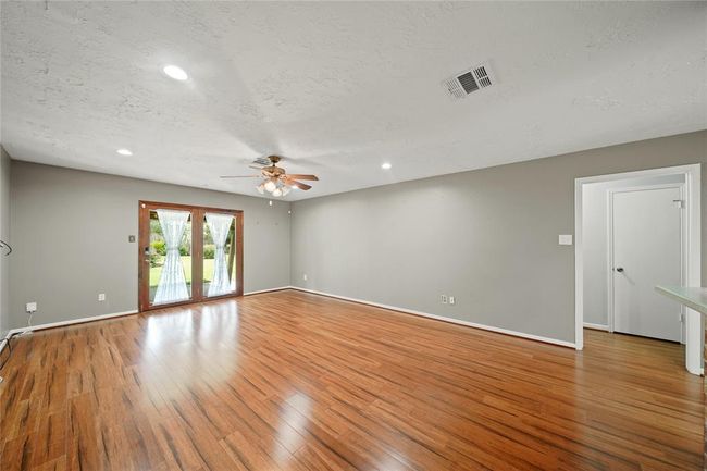 Spacious living area with double doors leading to covered patio. Opening pictured leads to the other two bedrooms and bathroom. | Image 11