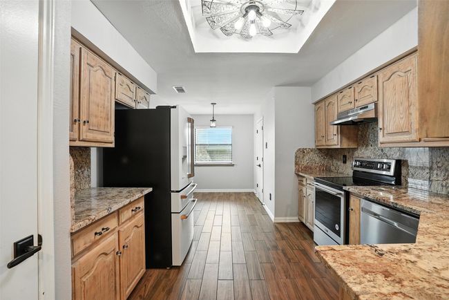 Kitchen featuring appliances with stainless steel finishes, under cabinet range hood, dark wood-style floors, decorative backsplash, and light stone countertops | Image 10
