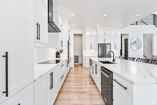 Kitchen featuring wall chimney exhaust hood, a sink, light wood-style floors, a spacious island, and stainless steel appliances | Image 58