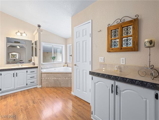 Bathroom with lofted ceiling, two vanities, wood finished floors, a bath, and a textured ceiling | Image 32