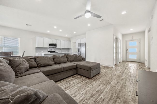 A different view of the spacious open-concept floor plan, showcasing the modern kitchen with white cabinets, and the flow from the entryway to the main living space. | Image 8