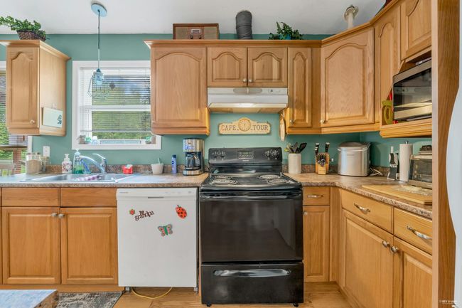 Kitchen with dishwasher, black electric range, under cabinet range hood, a sink, and stainless steel microwave | Image 22
