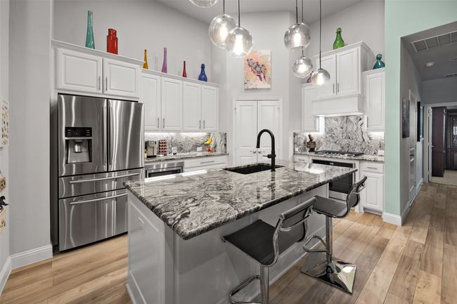 Kitchen with appliances with stainless steel finishes, a sink, light stone counters, white cabinetry, and tasteful backsplash | Image 7