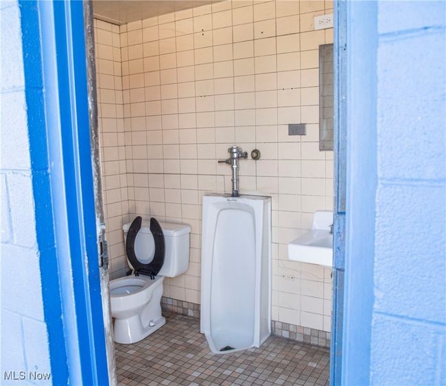 Bathroom with toilet, tile patterned floors, tile walls, and sink | Image 14