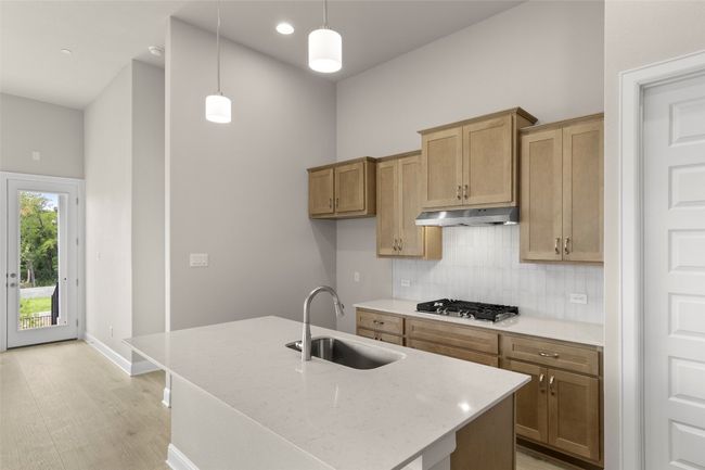 Kitchen with a sink, stainless steel gas stovetop, under cabinet range hood, decorative backsplash, and a high ceiling | Image 16