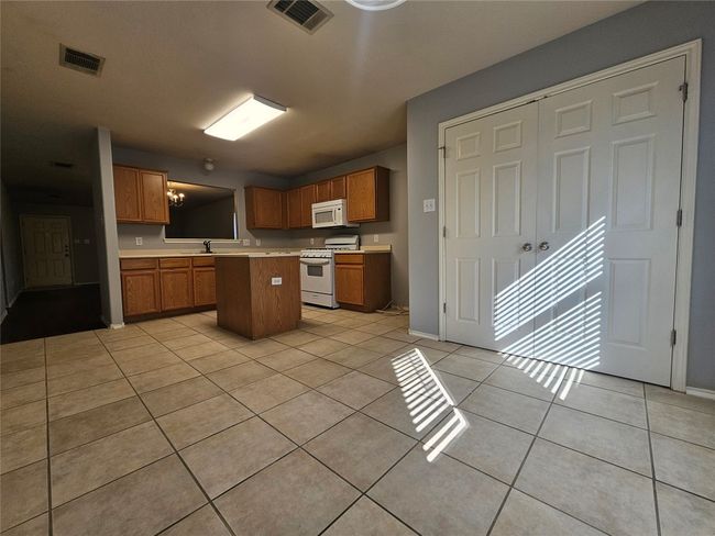Kitchen featuring white appliances, light countertops, light tile patterned floors, and brown cabinetry | Image 10