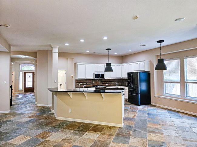 Kitchen featuring black fridge, stainless steel microwave, dark countertops, stone tile flooring, and baseboards | Image 10
