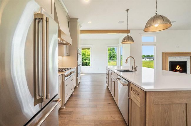 Kitchen featuring appliances with stainless steel finishes, a sink, custom range hood, hardwood / wood-style flooring, and light countertops | Image 27