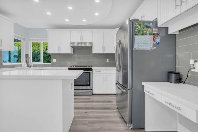 Kitchen with under cabinet range hood, decorative backsplash, white cabinets, and appliances with stainless steel finishes | Image 9