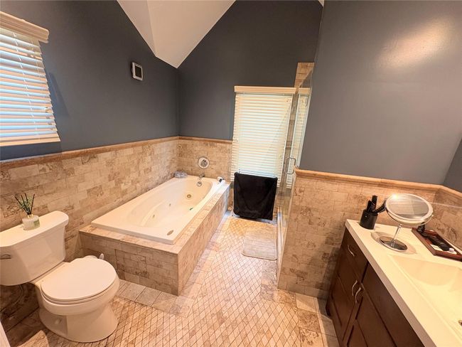 Full bathroom featuring tile walls, wainscoting, a stall shower, toilet, and a tub with jets | Image 11
