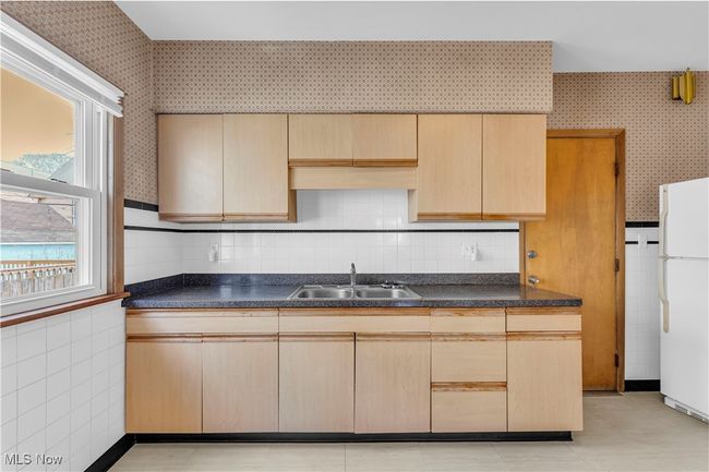 Kitchen featuring a healthy amount of sunlight, wallpapered walls, freestanding refrigerator, and a sink | Image 12