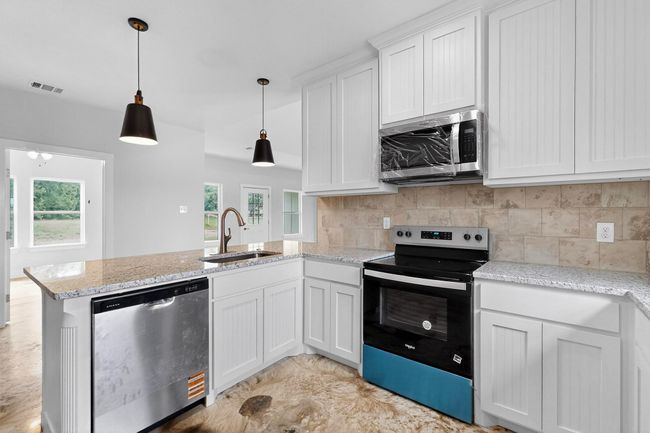 Kitchen featuring stainless steel appliances, a peninsula, backsplash, and white cabinetry | Image 22
