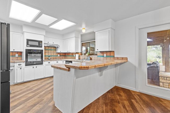 Kitchen with black appliances, white cabinetry, kitchen peninsula, tile countertops, and hardwood / wood-style flooring | Image 11